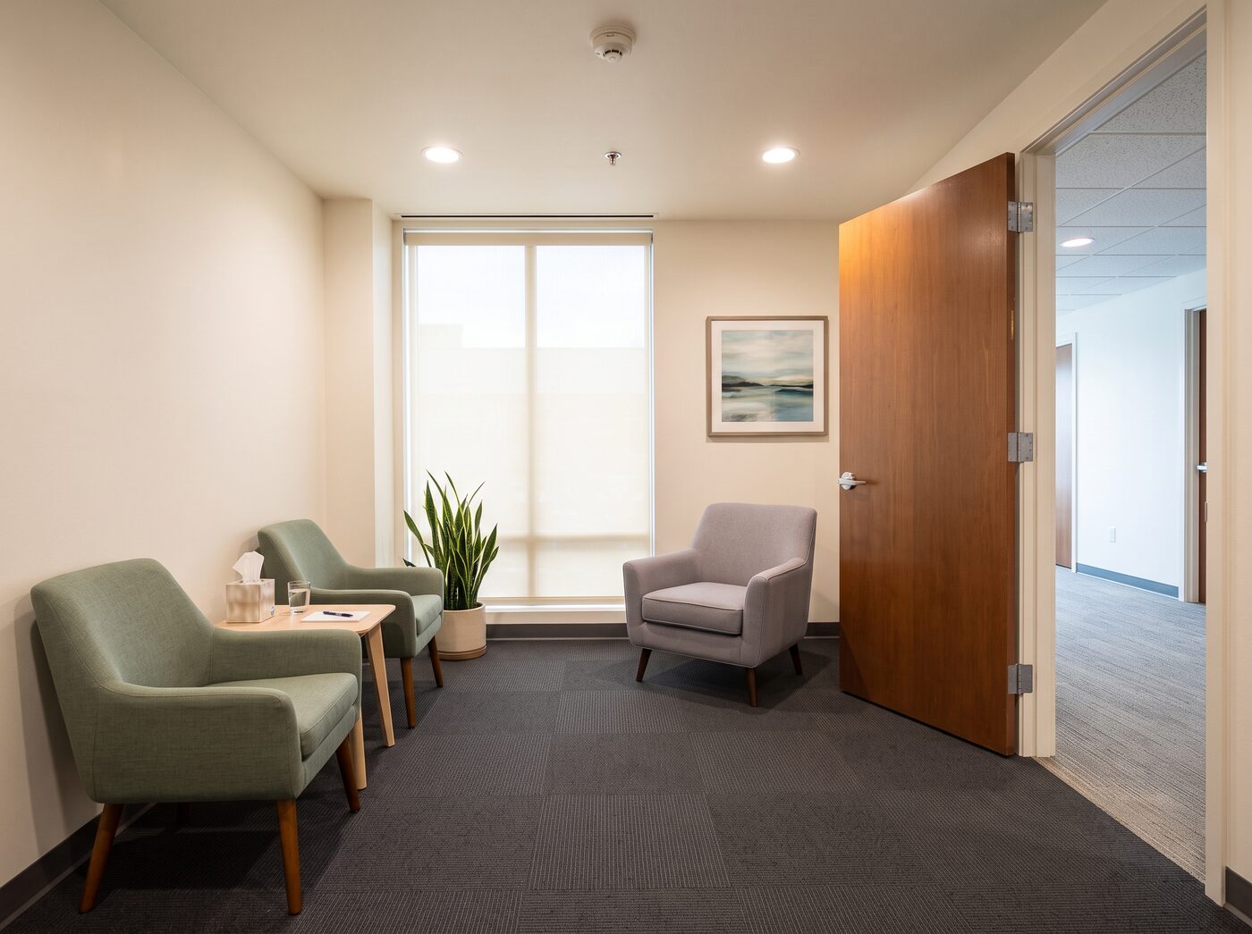 A spotless therapy consultation room with armchairs and a view down the office corridor